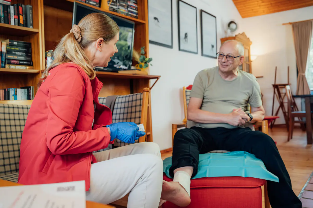 Wundprofi versorgt älteren Patienten mit Beinverband bei Hausbesuch.